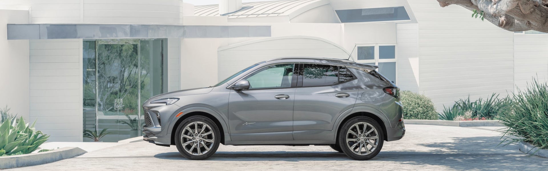 A silver 2024 Buick Encore GX Avenir parked in front of a modern house.